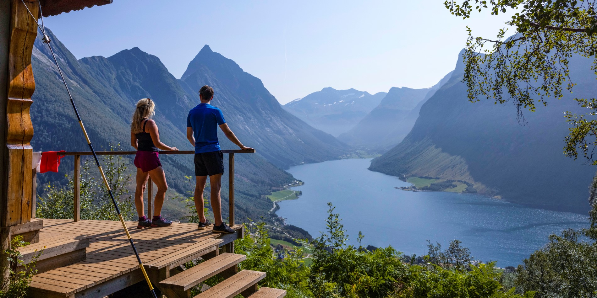 A couple is standing on a viewpoint overlooking Hjørundfjord. Vestcoast, Norway